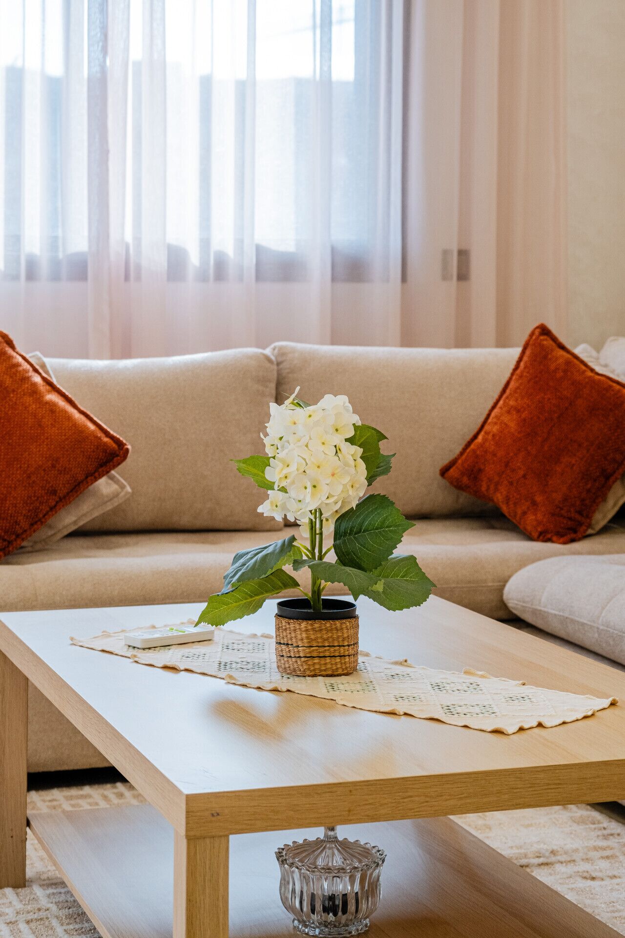 Een woonkamer met een bank, een salontafel en een vaas met witte bloemen.