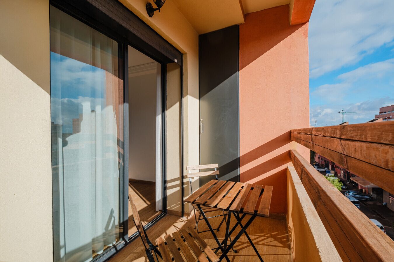 Een balkon met een houten tafel en stoelen, een schuifdeur en uitzicht op de stad.
