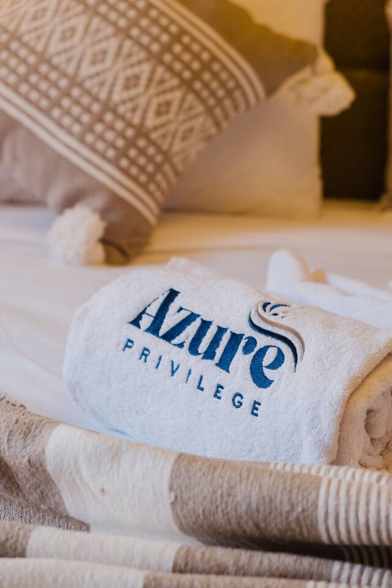 A neatly folded towel with the text "Azure Privilege" on it, placed on a bed with a patterned pillow and striped bedding.