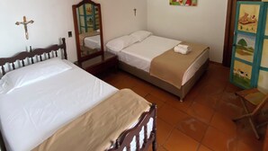 Una habitación con dos camas, cabecera de madera, una mesita, una lámpara de pared, un cuadro y una puerta de madera con un panel de cristal.