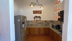 Una cocina con salpicadero de azulejos, armarios de madera, un refrigerador, una lámpara colgante y un adorno en la pared.