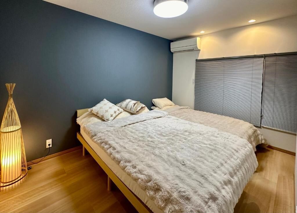A bedroom with a bed, a bedside lamp, and a window with blinds.