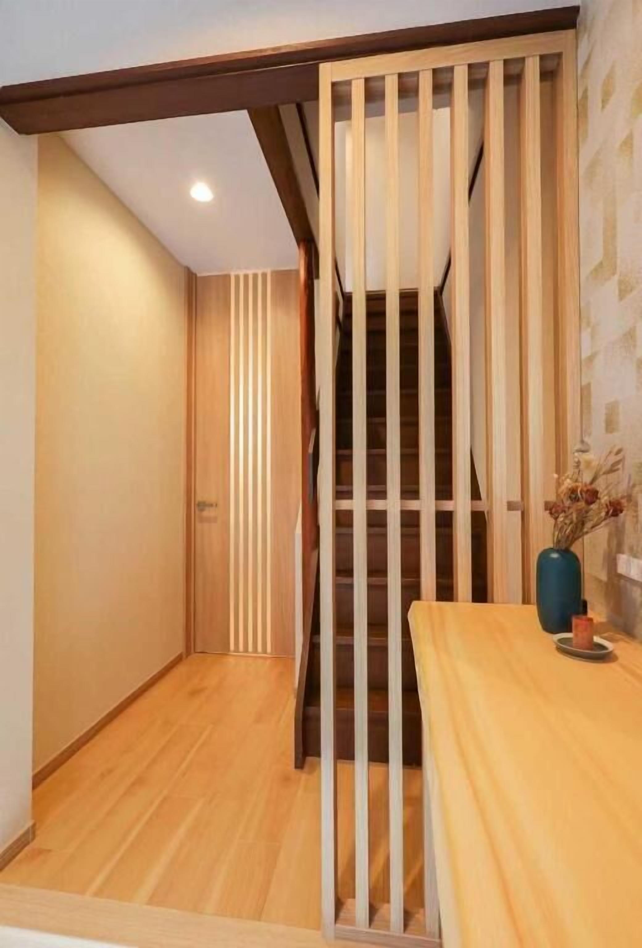 A wooden staircase with vertical slats, a wooden floor, and a small table with a vase and a candle.