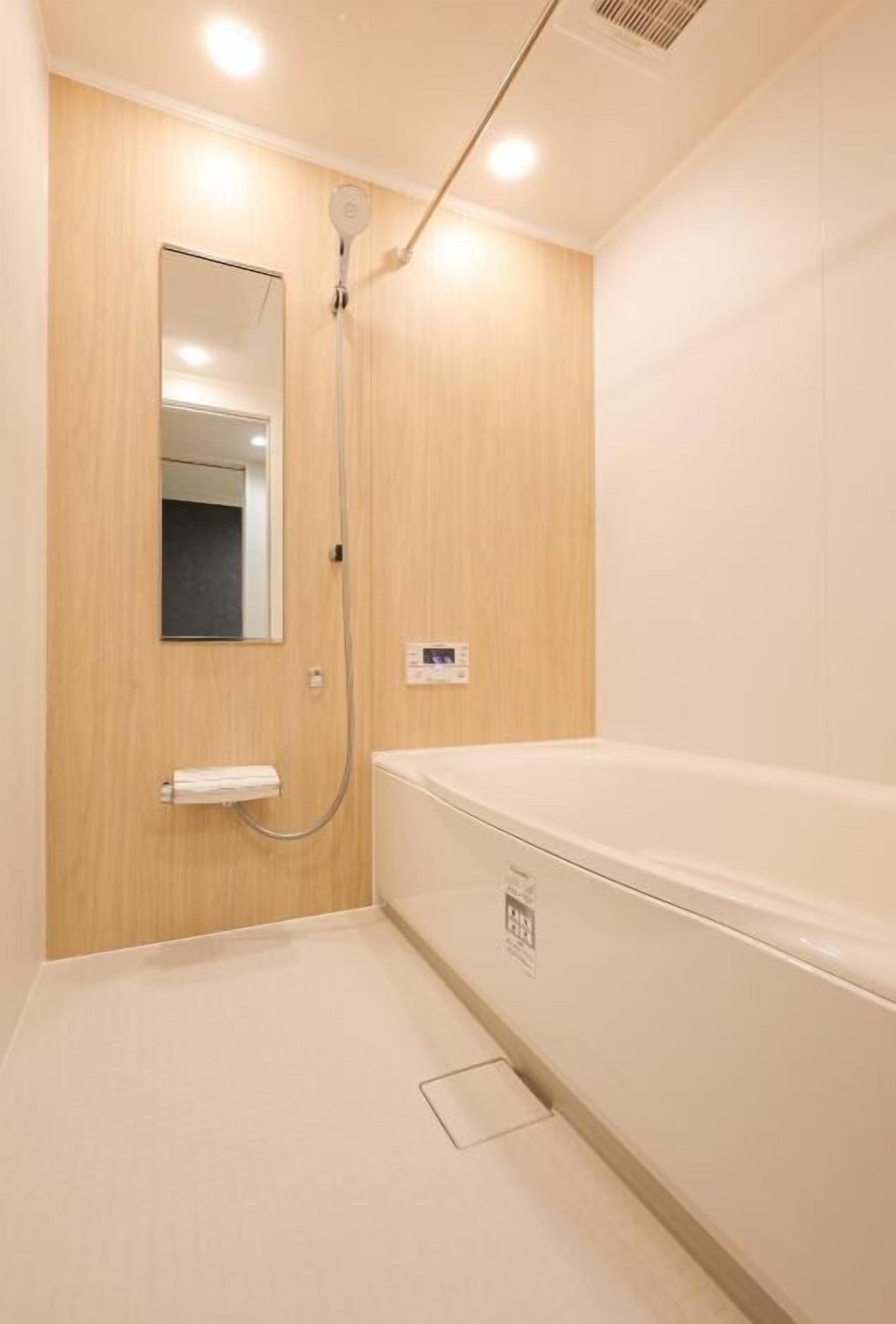 A small, modern bathroom with a wooden vanity, a white bathtub, and a mirror.