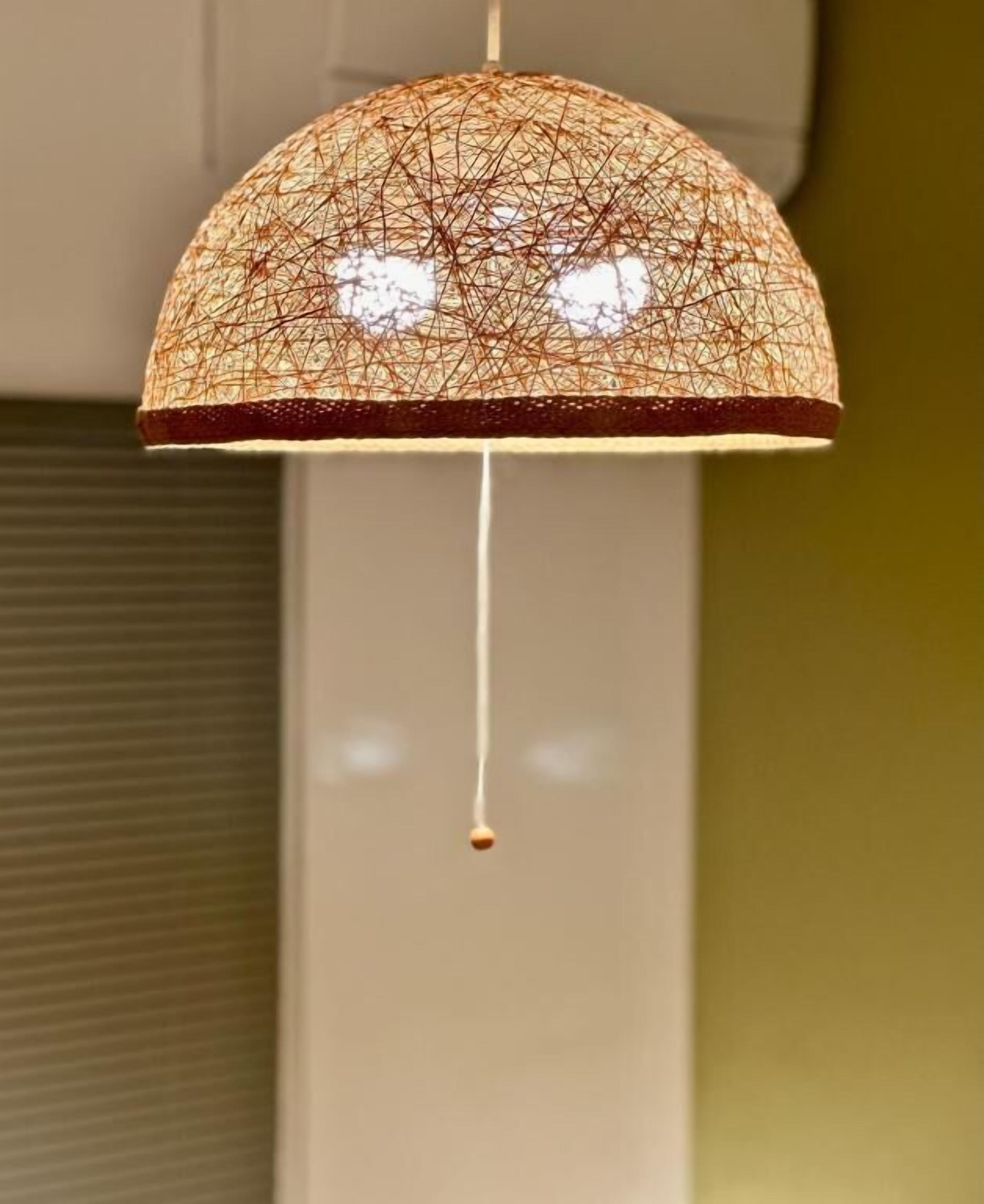A hanging lamp with a woven shade and a single droplet of water hanging from it.