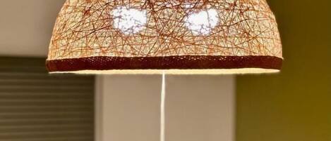 A hanging lamp with a woven shade and a single droplet of water hanging from it.