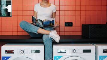 A person sitting on top of two stacked washing machines in a room with red tiled walls.