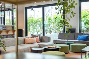 Un salón moderno con un sofá, otomanas, una mesita y grandes ventanales con vistas a zonas verdes.