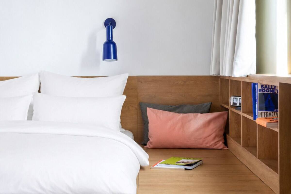 A modern bedroom with a wooden bed, a nightstand, a blue lamp, and a bookshelf with books.