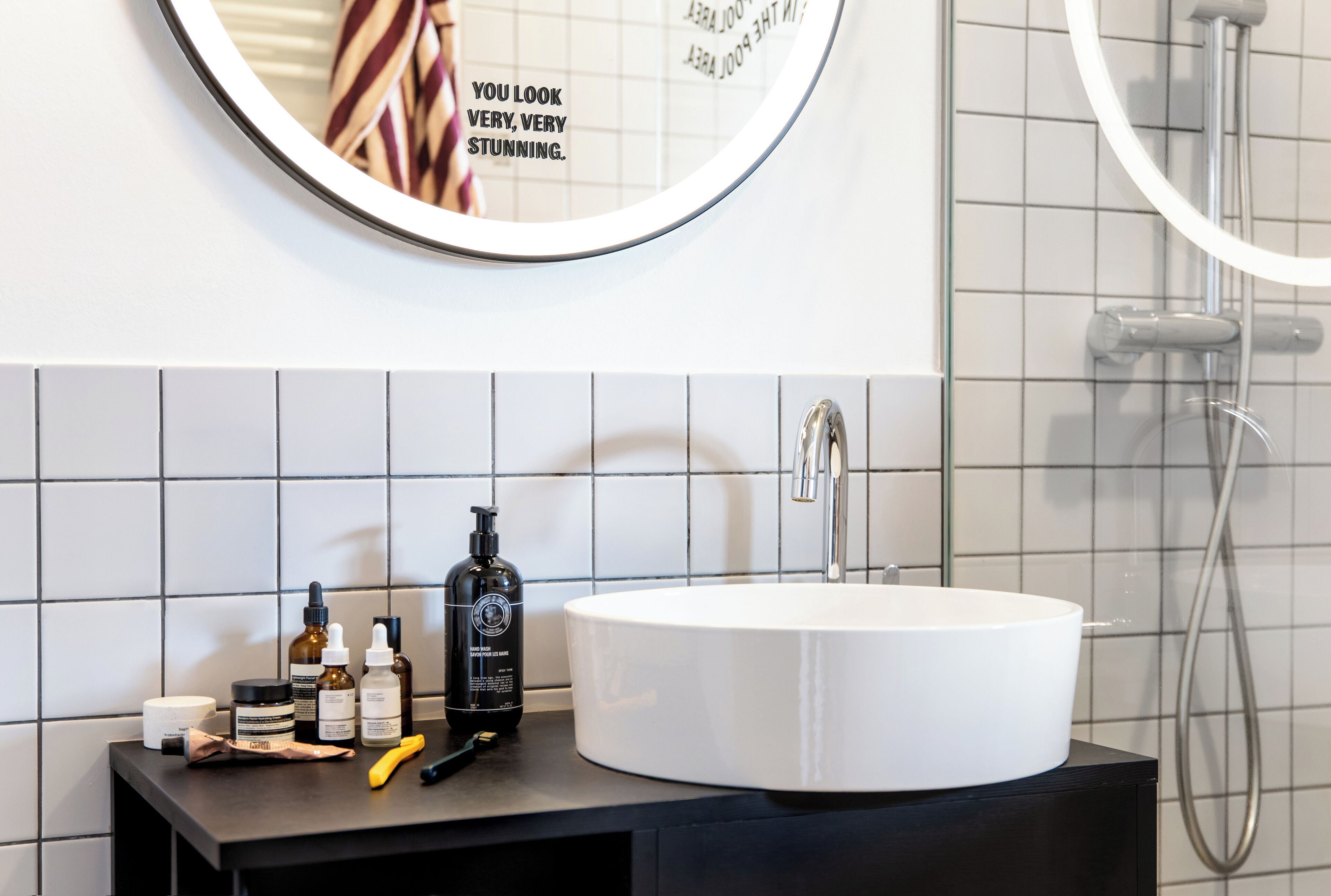 A bathroom with a round mirror, a white sink, and a shower.
