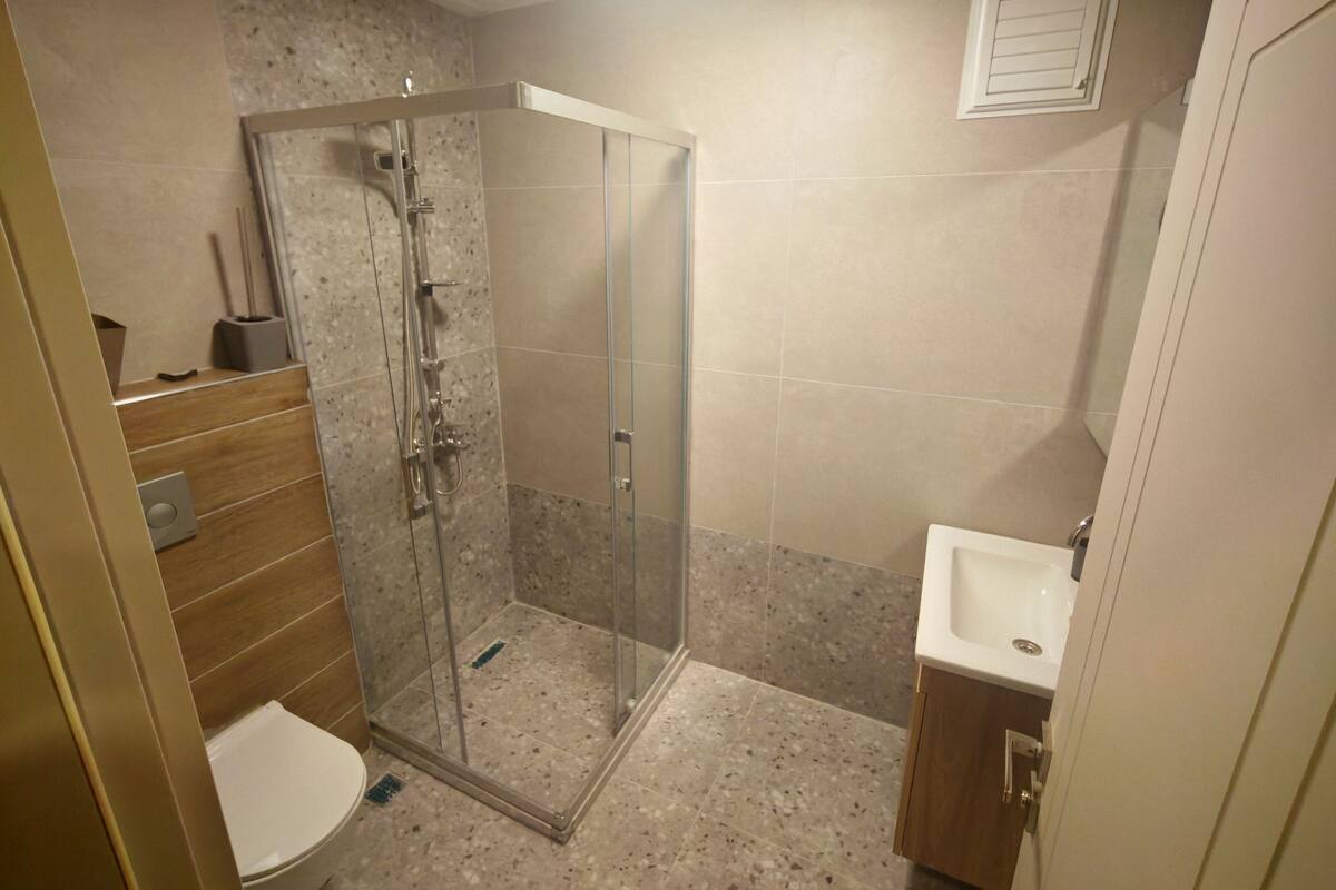 A bathroom with a glass-enclosed shower, a toilet, and a sink.