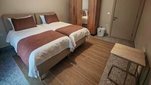 A hotel room with two beds, a wooden wardrobe, a small table, and a door. - Suitev (Arnavutkoy)