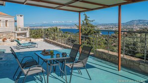 A terrace with a table and chairs, a pool, and a scenic view of a city and mountains. - Viewtifull-Villas 2 – Private Pool, Playground & Panoramic Views Near Heraklion (CRETE)