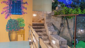 A staircase with stone walls and a wooden railing, leading to a balcony with a view of a windmill. - Viewtifull-Villas 2 – Private Pool, Playground & Panoramic Views Near Heraklion (CRETE)