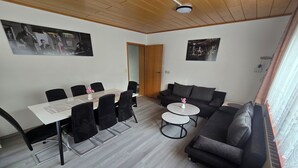 A modern living room with a dining area, featuring a wooden ceiling, grey flooring, black furniture, and two round tables. - Vacation home Lautertal-Lodge with private pool/whirlpool for up to 10 people (Kreimbach-Kaulbach)