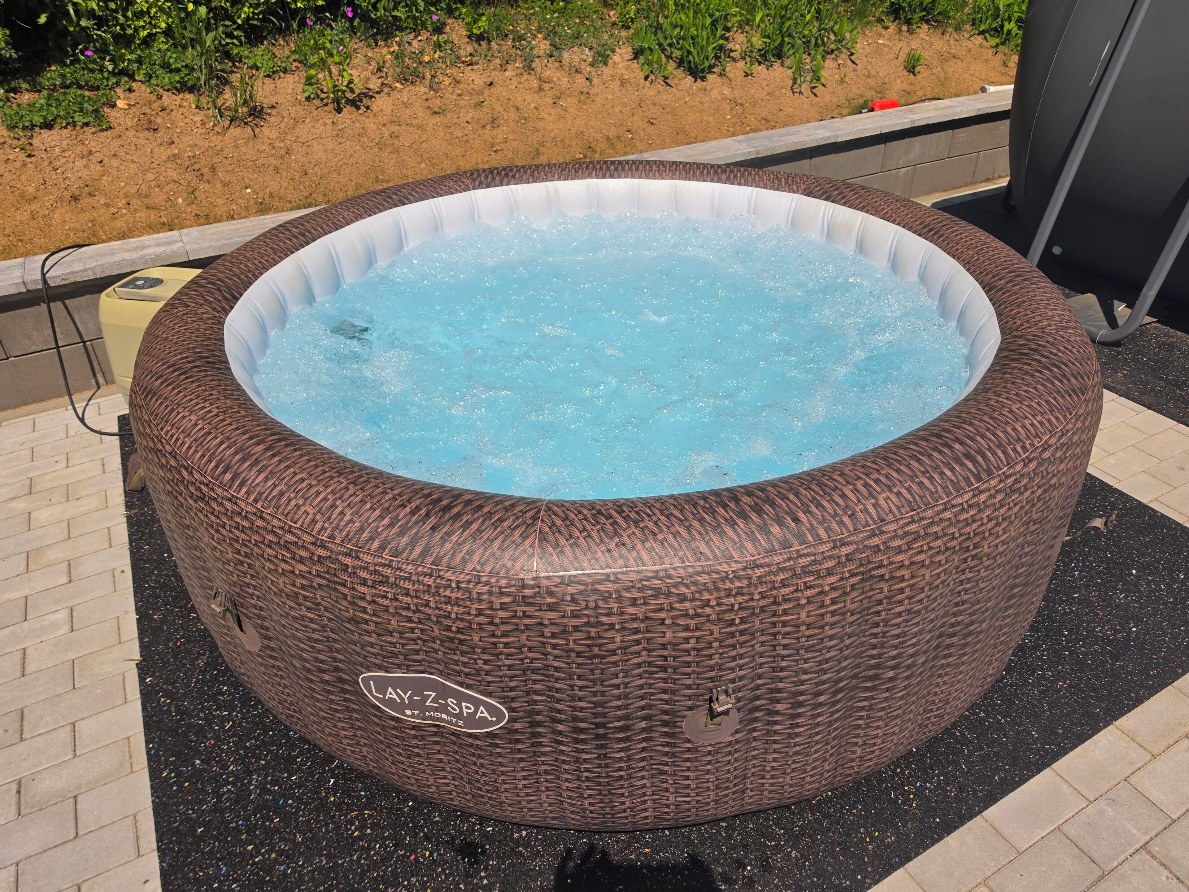 A large, round, wicker hot tub with a label 'LAY-Z-SPA ST. MORITZ' on its side, placed outdoors on a paved surface.