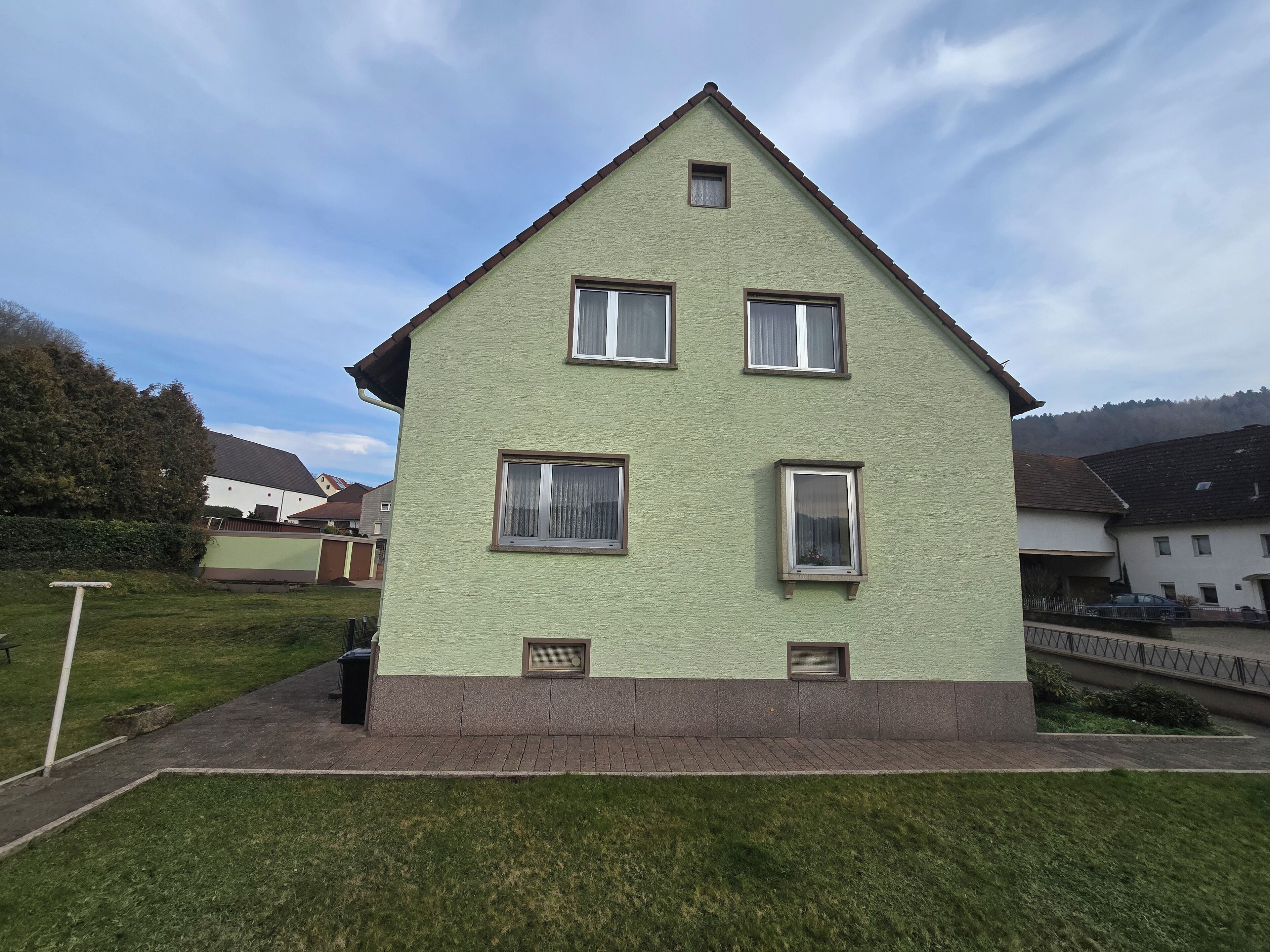A two-story house with a green facade, multiple windows, and a small balcony.