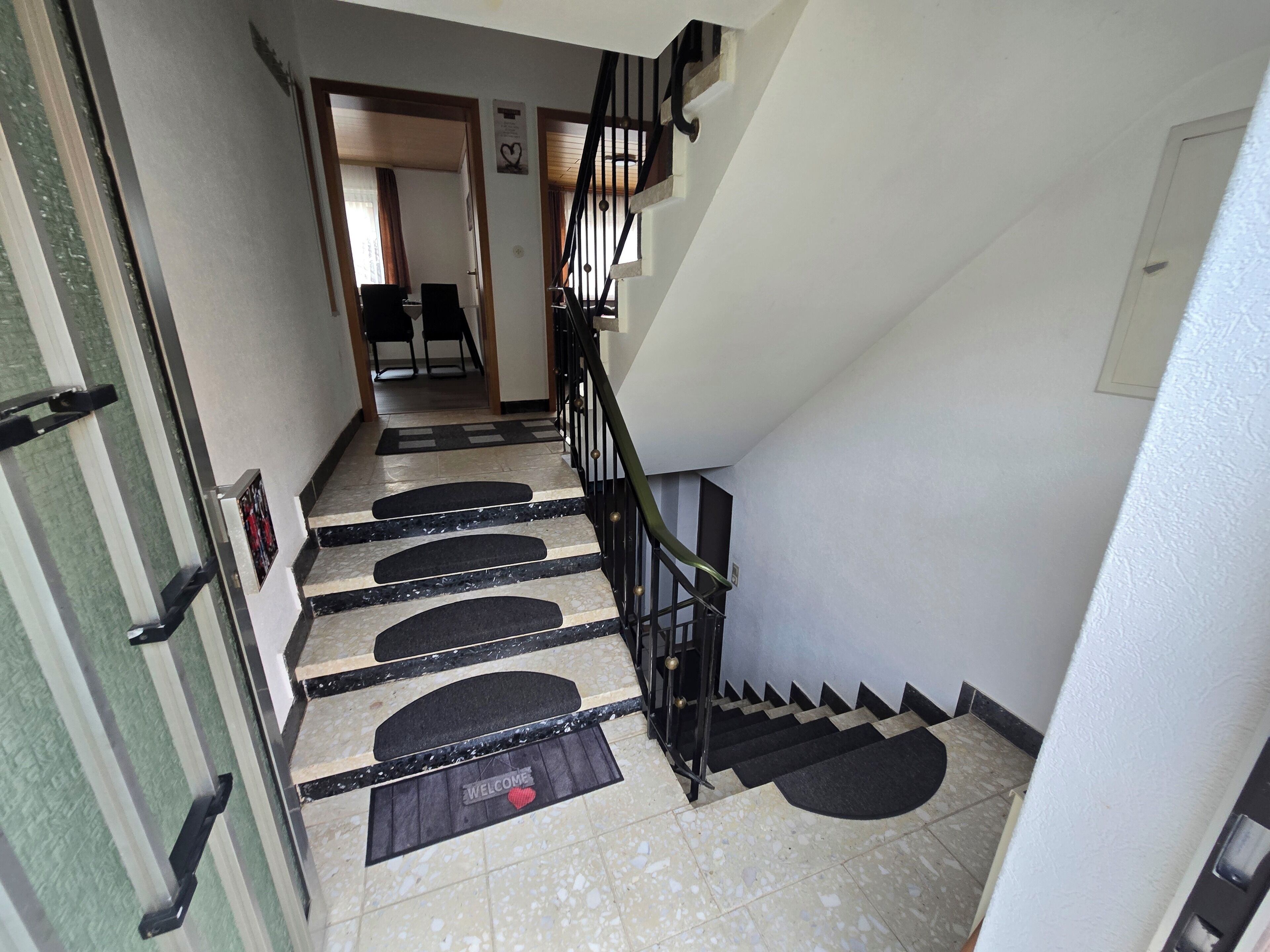 A staircase with black handrails and a 'WELCOME' mat at the bottom.