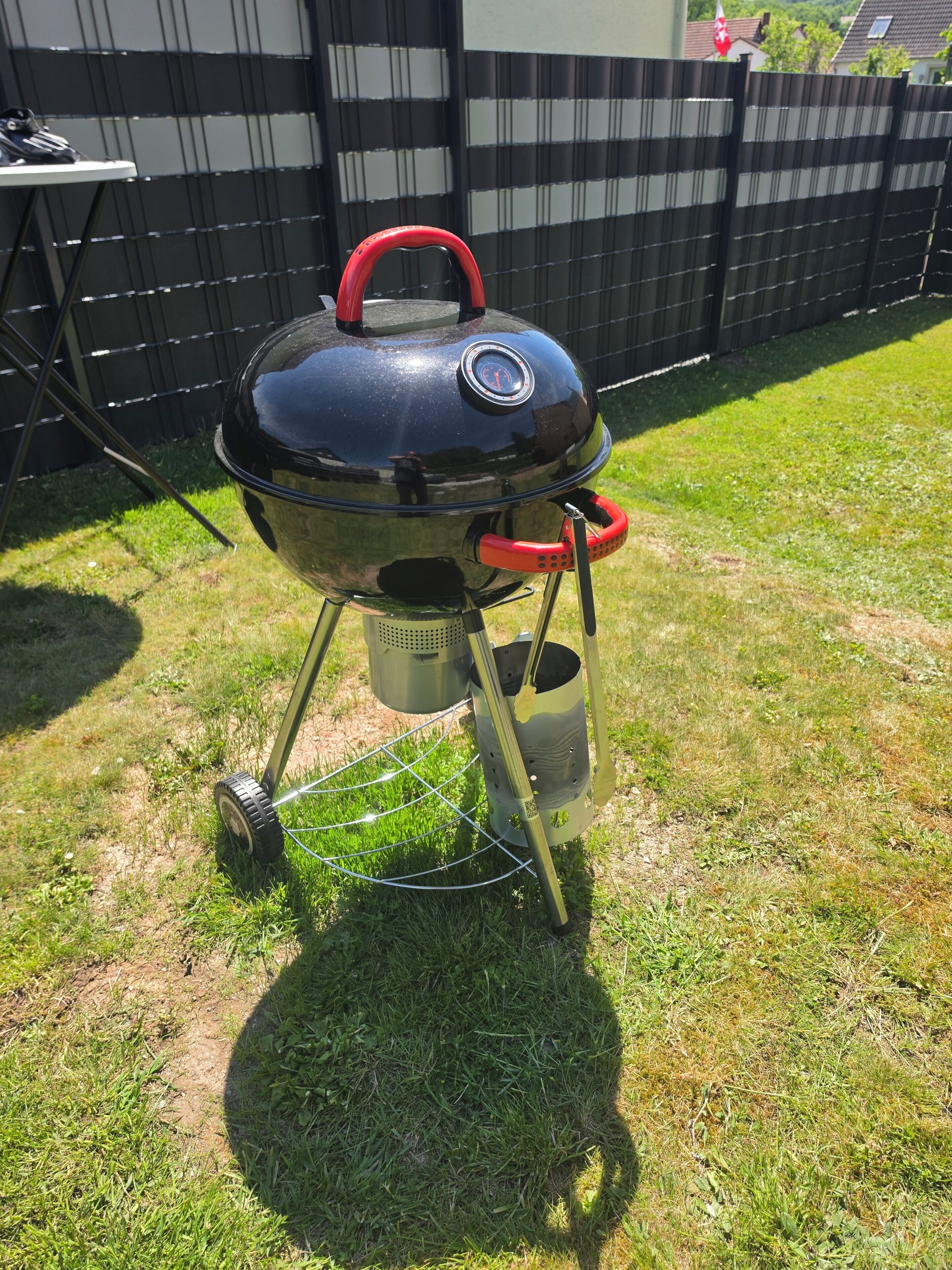 Ein tragbarer Grill mit digitalem Thermometer auf einer grünen Rasenfläche.