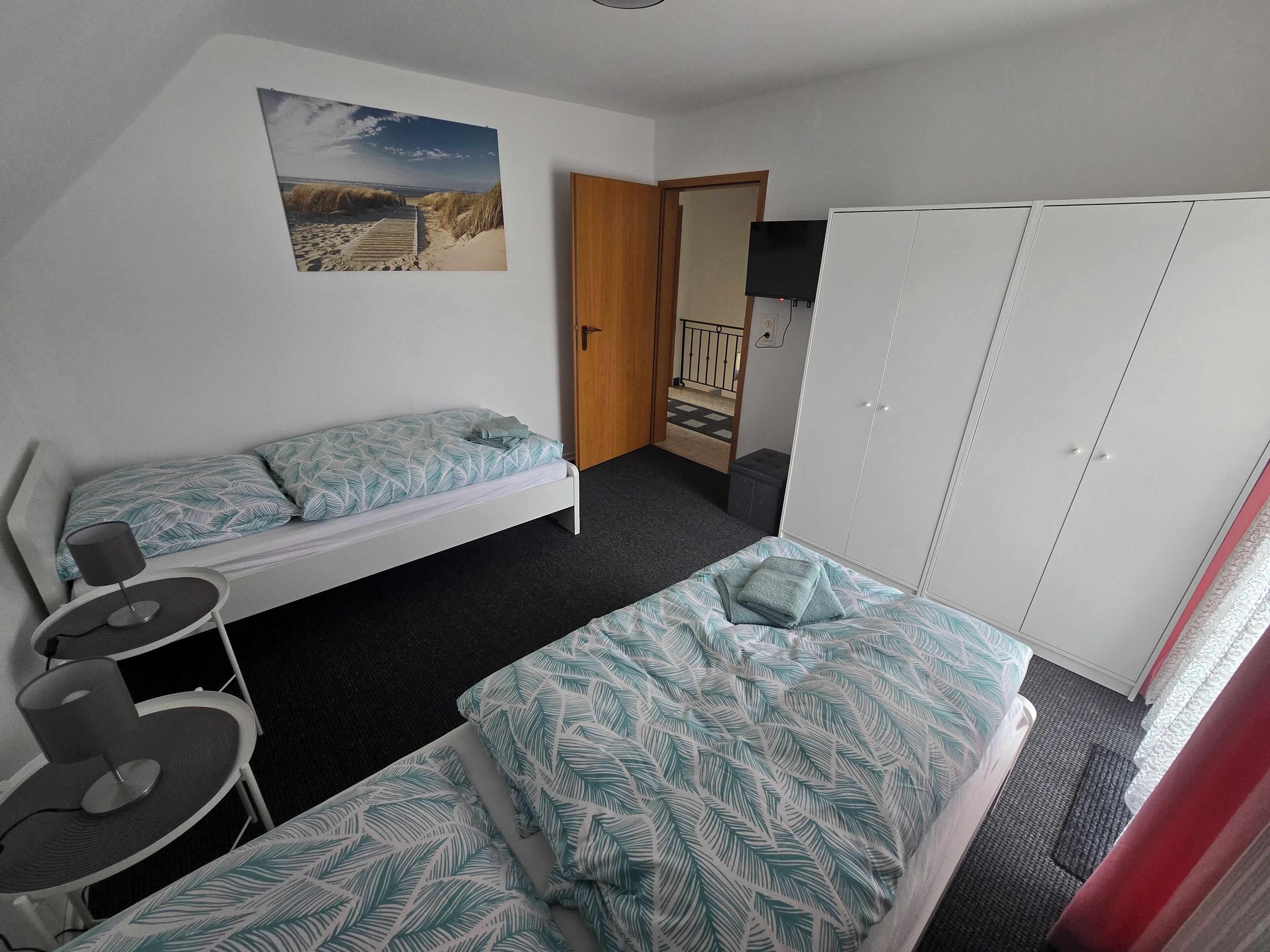 Un dormitorio con dos camas individuales, un escritorio, una silla, un armario y una puerta que da a un balcón.