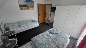 Un dormitorio con dos camas individuales, un escritorio, una silla, un armario y una puerta que da a un balcón.