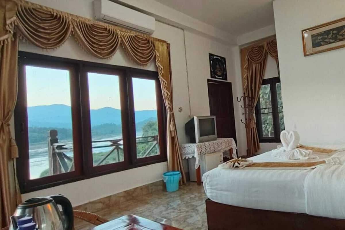 A hotel room with a bed, a desk with a computer, a window with curtains, and a view of mountains.