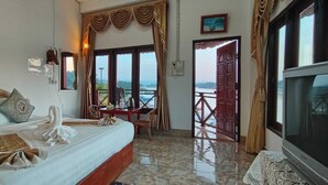 A hotel room with a bed, a table, a chair, a TV, and a balcony with a view. - Phonevichith Riverside Hotel Houayxai (Houayxay)
