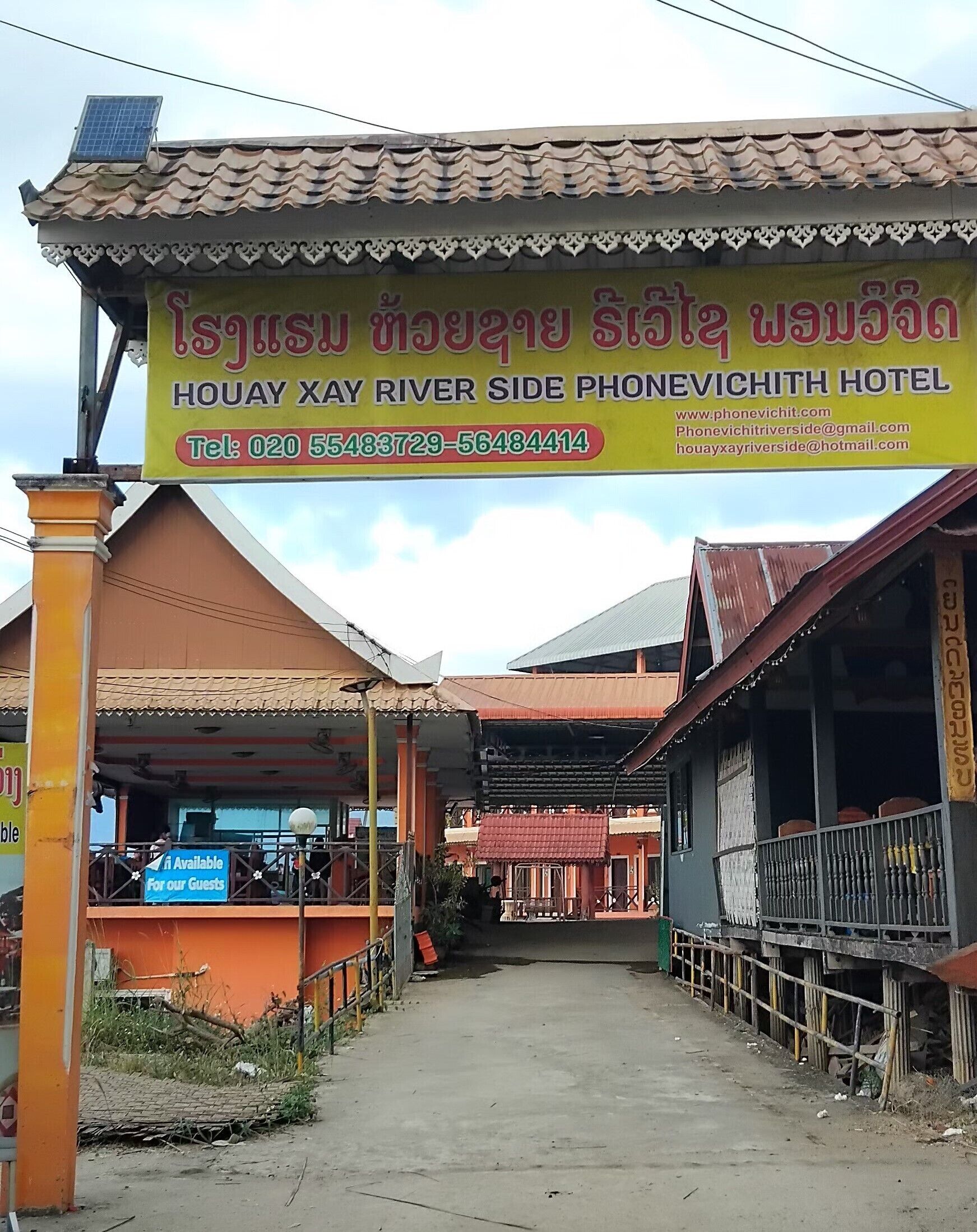 A hotel with a signboard in a local language, a covered walkway, and a building with a tiled roof.