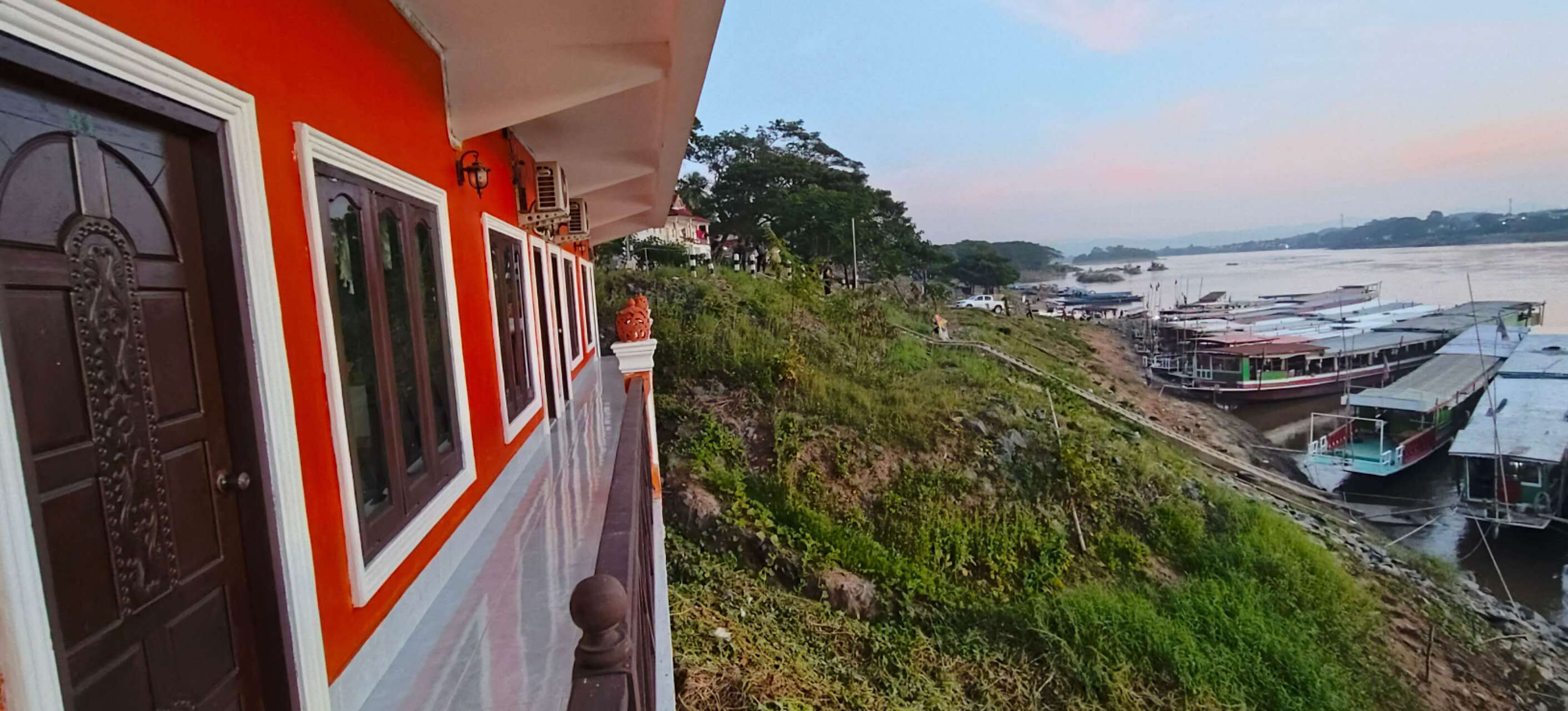 Ein Gebäude mit roter Fassade und einem Balkon mit Blick auf einen Fluss und Boote.
