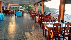 An indoor dining area with tables and chairs, a tiled floor, and a view of the sea through large windows. - Phonevichith Riverside Hotel Houayxai (Houayxay)