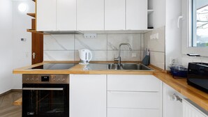 A modern kitchen with white cabinets, a stainless steel sink, a kettle, and a microwave. - Apartment Josef with Private Terrace (Radolfzell am Bodensee)