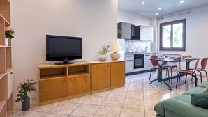 Un salon moderne doté d’un téléviseur à écran plat, de meubles en bois, d’un canapé vert et d’un coin repas avec une table et des chaises.