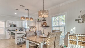 A modern kitchen with white cabinets, stainless steel appliances, and a central island. There are wicker chairs and a dining table with a chandelier. - Family Friendly & Resort Perks! Perdido Key Condo (Pensacola)