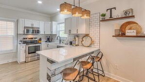 A modern kitchen with white cabinetry, a large island with bar stools, a built-in oven, and a hanging light fixture. - Family Friendly & Resort Perks! Perdido Key Condo (Pensacola)