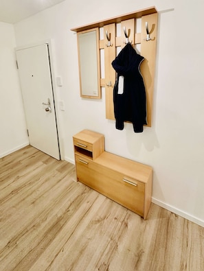 A room with a wooden bench, a coat rack with hooks, a mirror, and a door. - Eastside Apartment Karlsruhe – stylish and peaceful living (Karlsruhe)