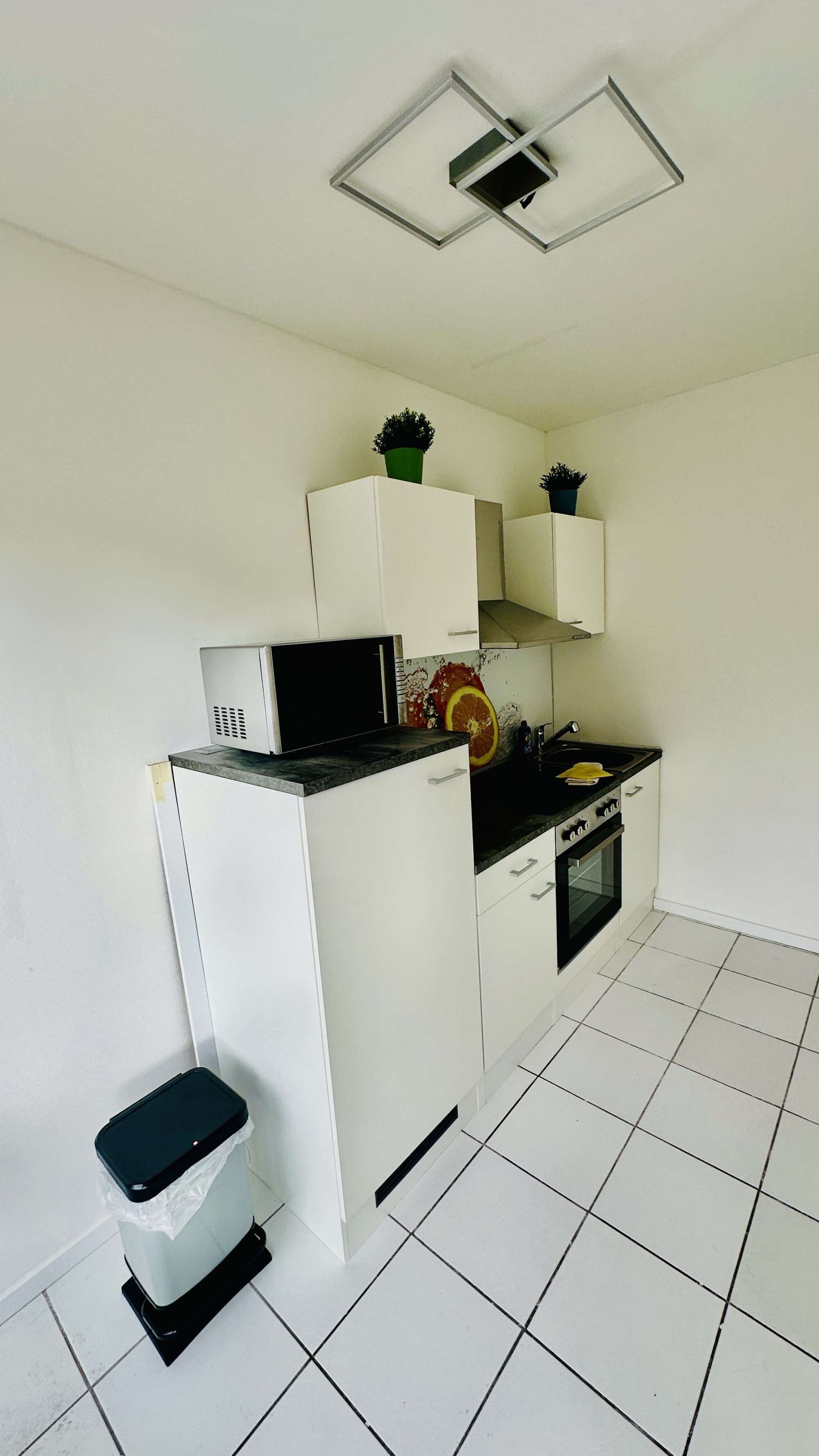 A compact kitchen with white cabinets, a black countertop, a microwave, a sink, and a small trash bin.