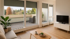 Ett modernt vardagsrum med en soffa, ett soffbord, en tv och stora fönster som ger utsikt över omgivningen.