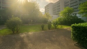 En stenlagd innergård med en gångstig av tegelstenar, omgiven av grönska och moderna byggnader.