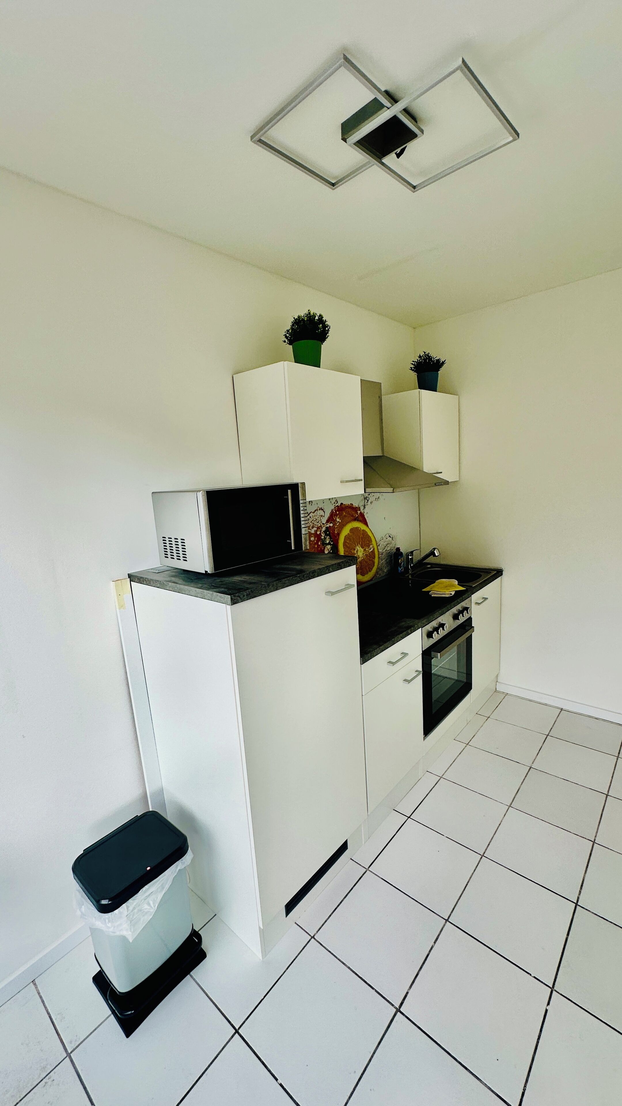 Une cuisine compacte avec des meubles blancs, un plan de travail noir, un four à micro-ondes, un évier et une petite poubelle.
