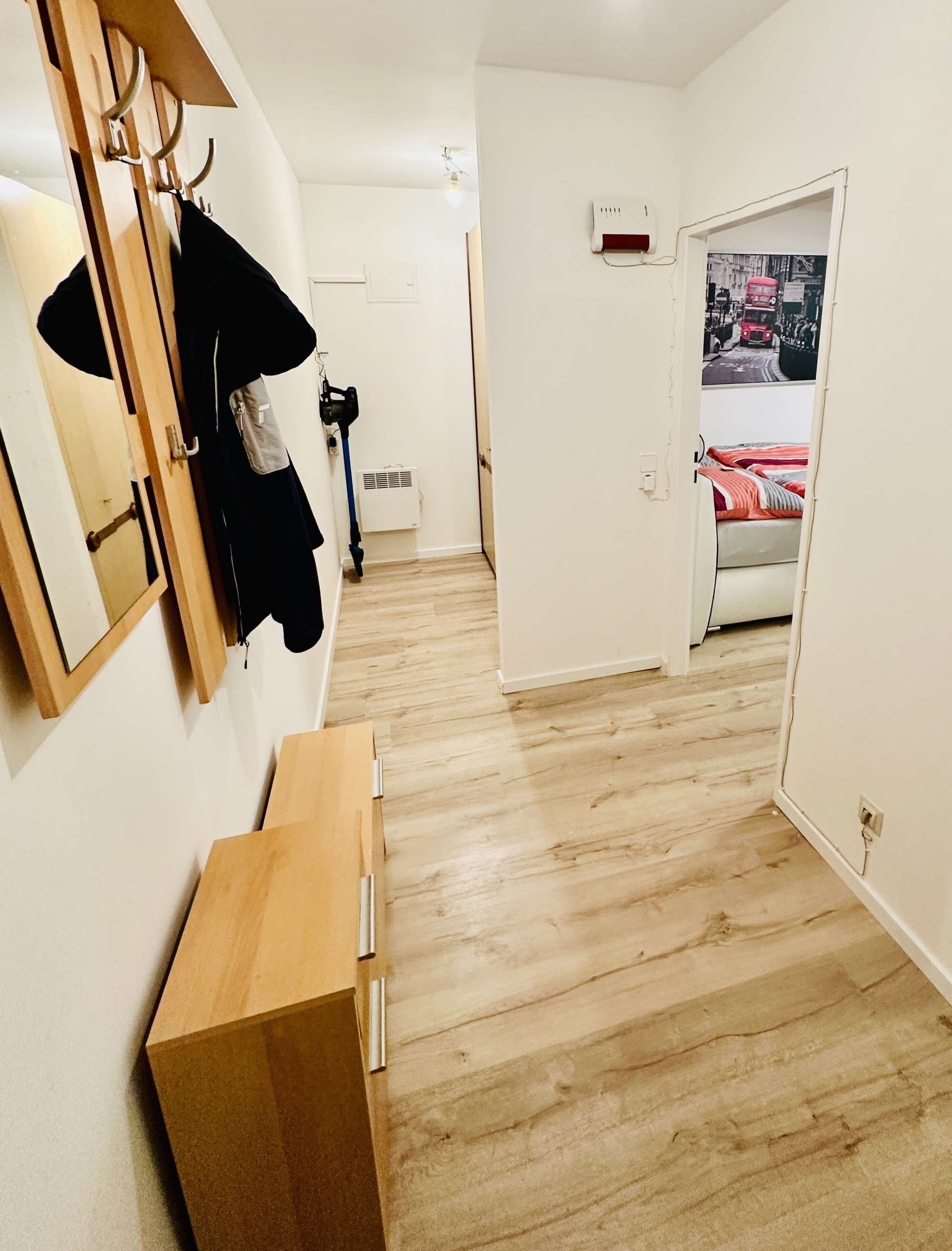 A hallway with a wooden bench, a coat rack with clothes, a door leading to a room with a bed, and a wall-mounted air conditioner.