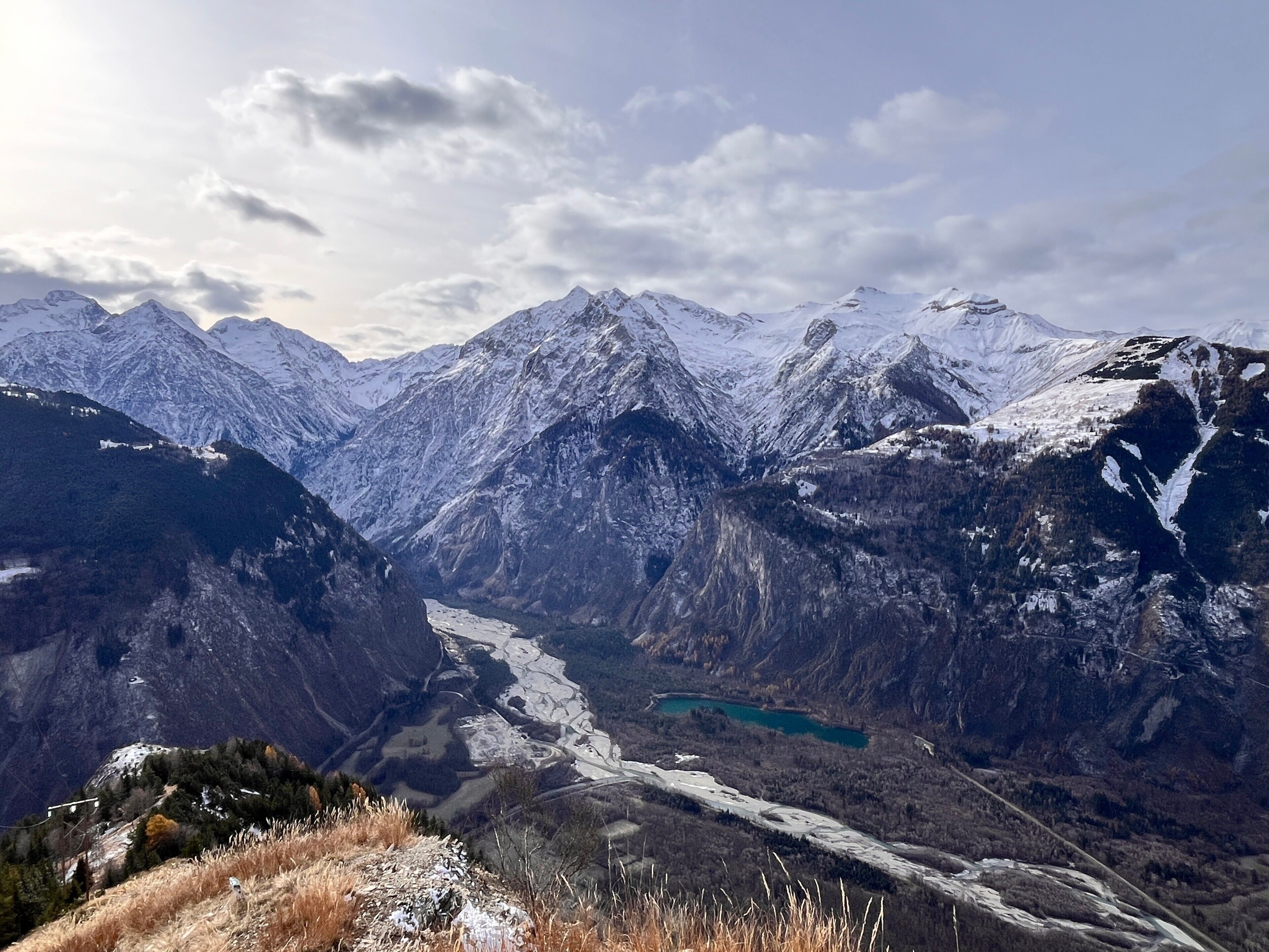 A mountainous landscape with snow-covered peaks, a valley with a river, and a distant lake.