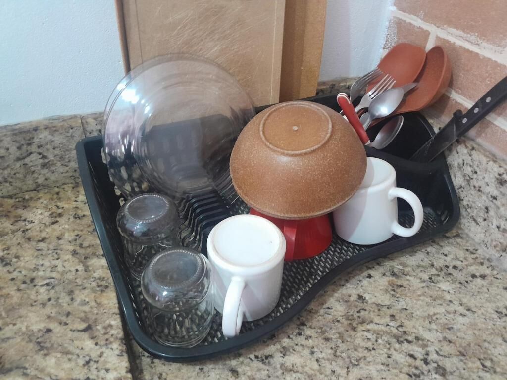 Un plan de travail de cuisine sur lequel se trouve un plateau noir contenant divers ustensiles, notamment un saladier en verre, une casserole rouge et plusieurs tasses blanches.
