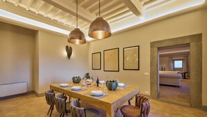 Un comedor con una mesa de madera, seis sillas, lámparas colgantes y cuadros en la pared.