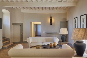 A modern living room with a sofa, coffee table, and decorative items. There is a lamp and framed artwork on the wall. - The Vagnucci Apartment combines traditional charm with modern comfort.   (Cortona)