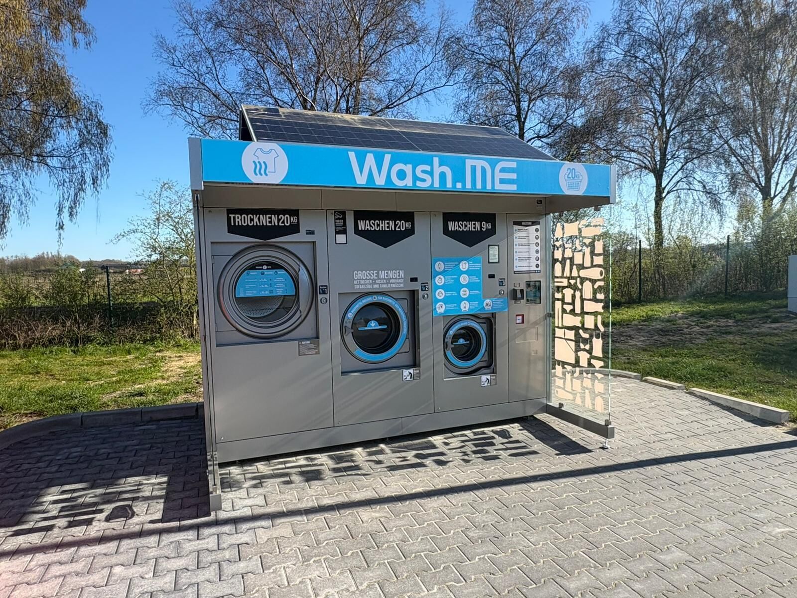 A public wash station with three washing machines, a solar panel, and a clear sky.