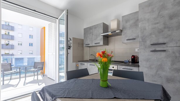 Una cocina moderna con armarios grises, una mesa de comedor con un florero y vistas a un balcón con sillas.