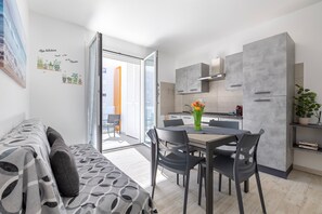 A modern kitchen with grey cabinets, a dining table with chairs, and a sofa with patterned cushions. - Apartment 'Brisa Blanca- Alghero' with Private Terrace, Wi-Fi and Air Conditioning (Alghero)