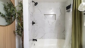 Une salle de bain moderne avec un mur de douche en marbre blanc, une étagère rectangulaire intégrée, une douchette noire et un rideau de douche vert.