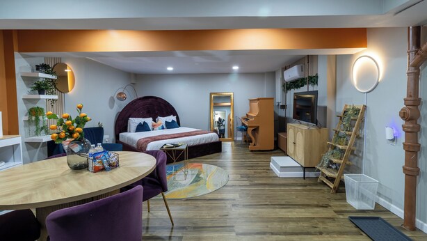 Une chambre moderne avec un lit, une table de chevet et un bureau avec une chaise. On y trouve également une commode, un téléviseur et une étagère avec des plantes.