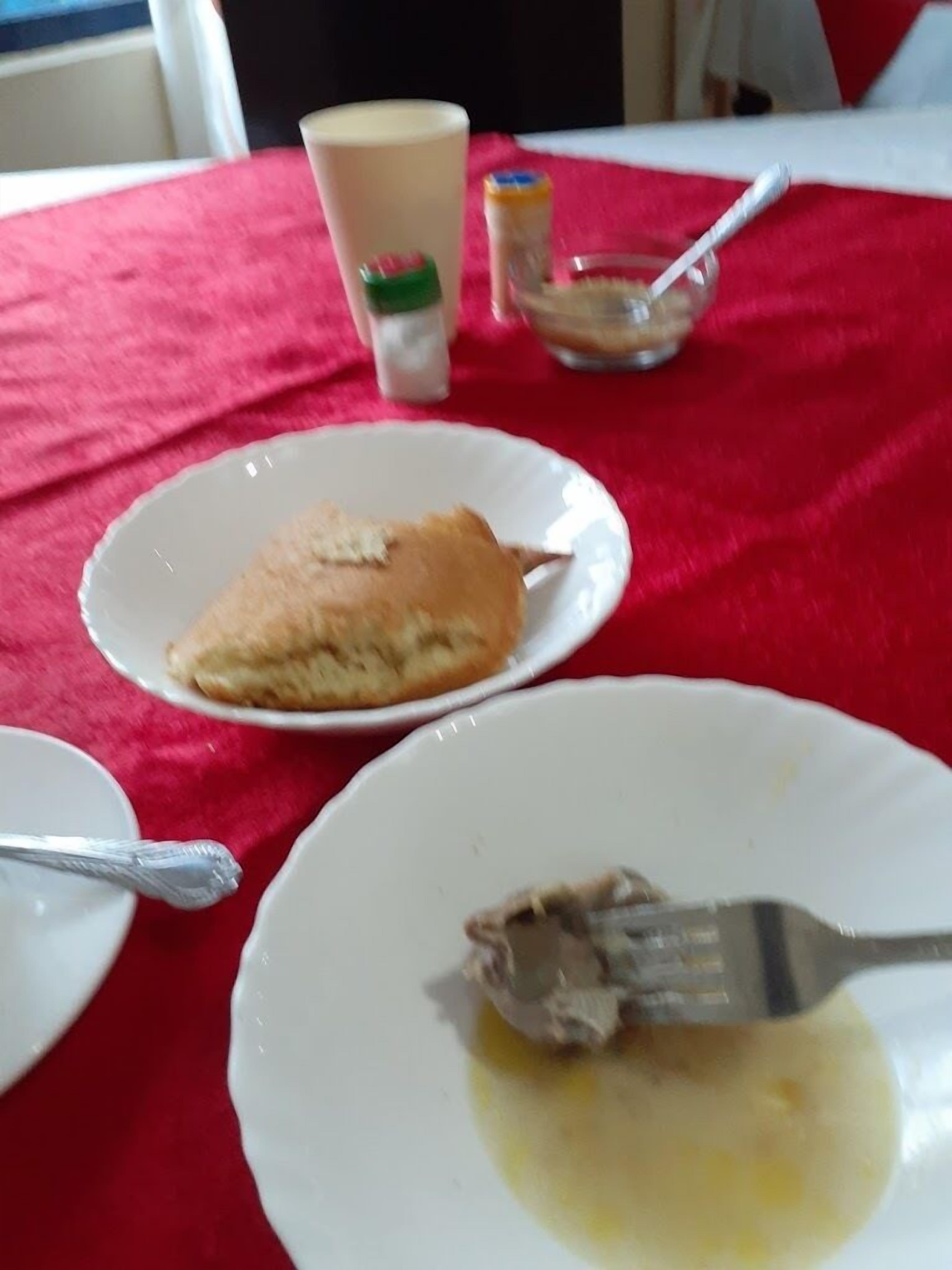 A table with a red tablecloth, a plate with a piece of food, a cup, and a small container with a spoon.